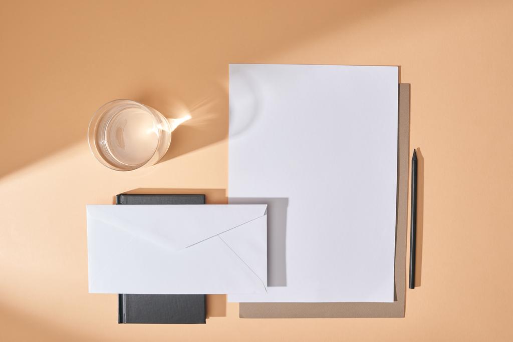 Kağıt, zarf, kalem, bir bardak su ve bej arkaplandaki not defterinin üst görünümü - Fotoğraf, Görsel
