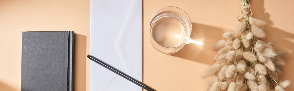 plano panorámico de cuaderno, sobre, pluma, vaso de agua y espiguillas lagurus sobre fondo beige
 - Foto, imagen