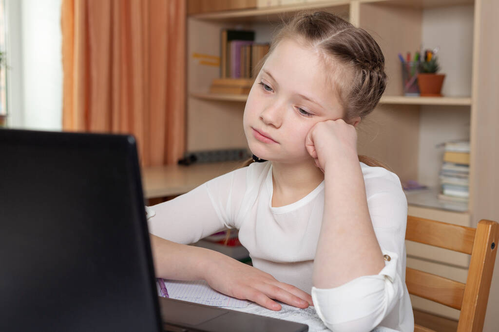 Vakava koulutyttö katsoo kannettavan tietokoneen näyttöä. Etäopetus verkossa, kotiopetus, kotiopetus, karanteenikäsittely - Kuva - Valokuva, kuva