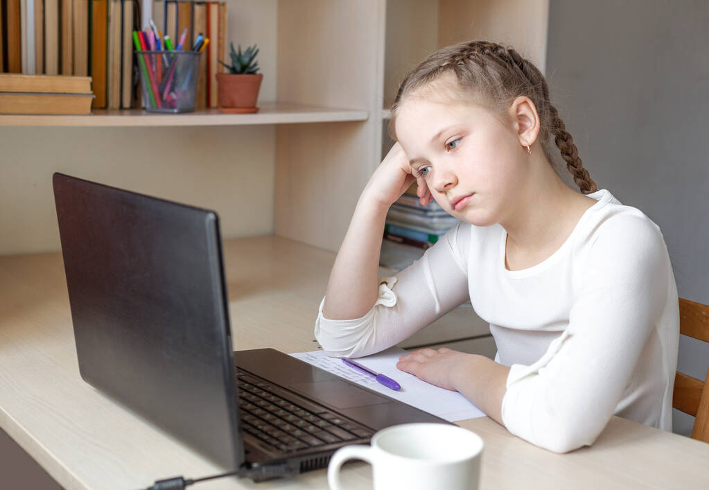 Серьёзная школьница смотрит на экран ноутбука. Дистанционное обучение онлайн, домашняя школа, домашнее образование, концепция карантина - Образ - Фото, изображение