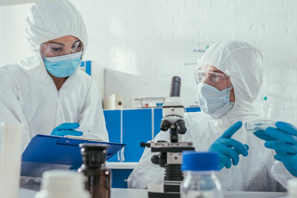 foco seletivo de dois bioquímicos segurando placas de Petri perto do microscópio e recipientes médicos
 - Foto, Imagem