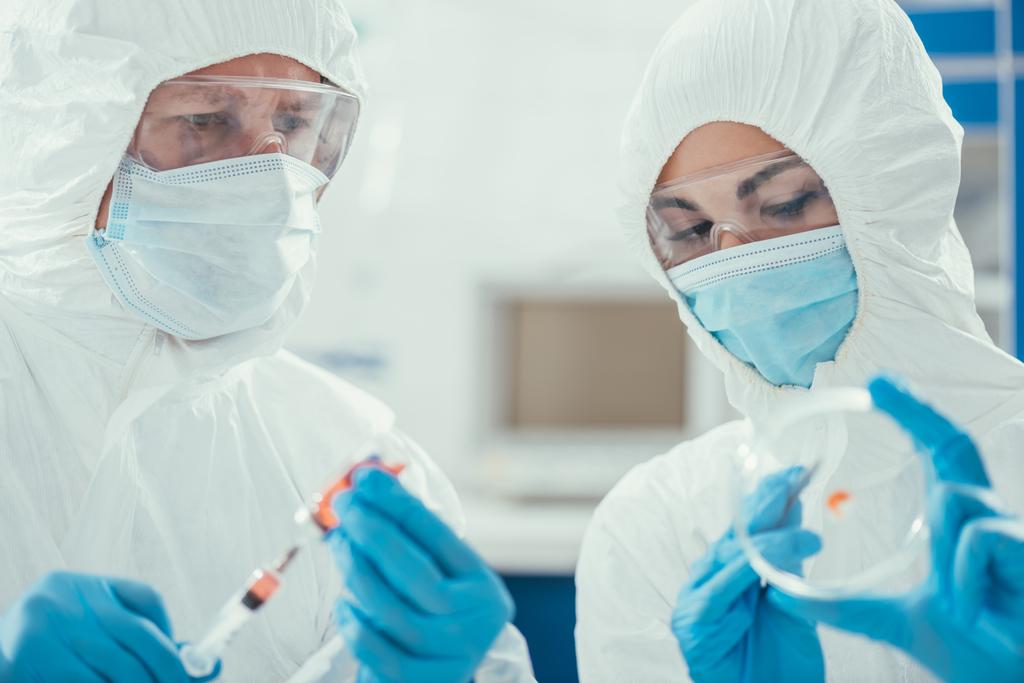 ペトリ皿を持っている同僚の近くに注射器で薬を飲む生化学者 - 写真・画像