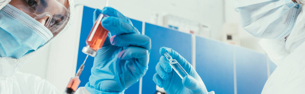 panoramatický záběr biochemika, který užívá léky s injekční stříkačkou poblíž ampule - Fotografie, Obrázek