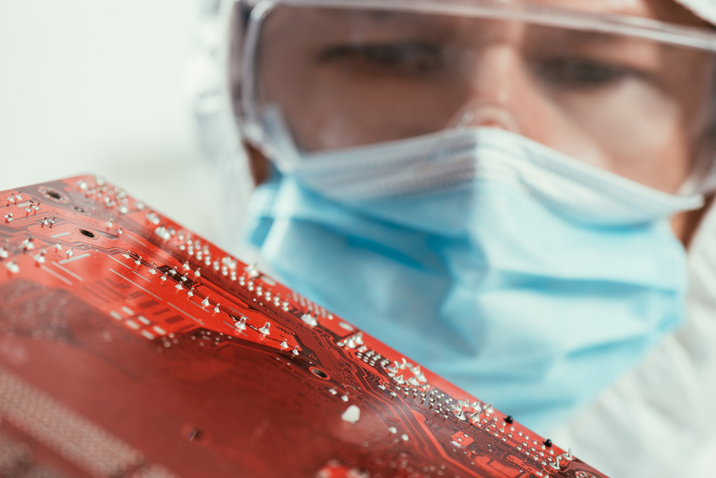 selective focus of engineer in medical mask and goggles holding computer motherboard - Photo, Image
