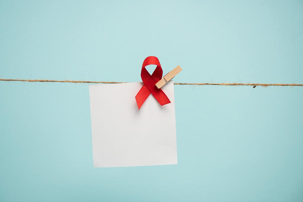 Κενή κάρτα με το AIDS ευαισθητοποίηση κόκκινη κορδέλα στο σχοινί με καρφίτσα που απομονώνονται στο μπλε  - Φωτογραφία, εικόνα