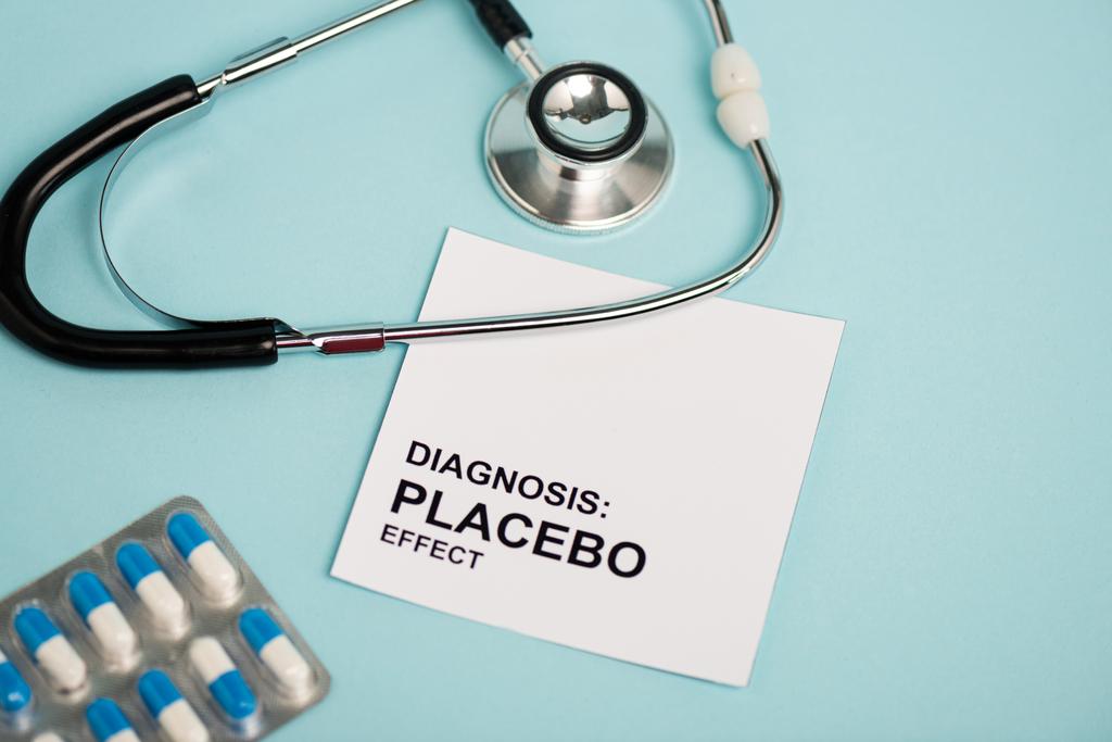 Tarjeta con letras de efecto placebo, pastillas y estetoscopio sobre fondo azul
 - Foto, Imagen