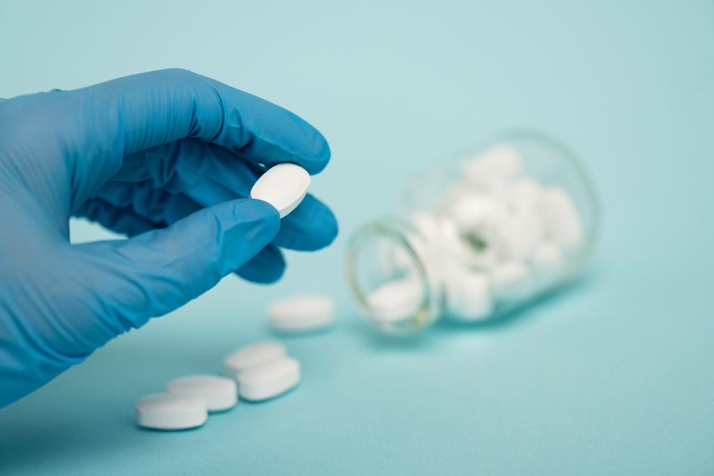 Nahaufnahme von Arzt hält Pille in der Nähe Glas auf blauem Hintergrund - Foto, Bild