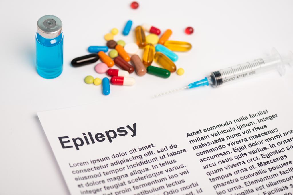 Бумага с надписью "эпилепсия" возле банки, шприца и таблеток на белом фоне - Фото, изображение