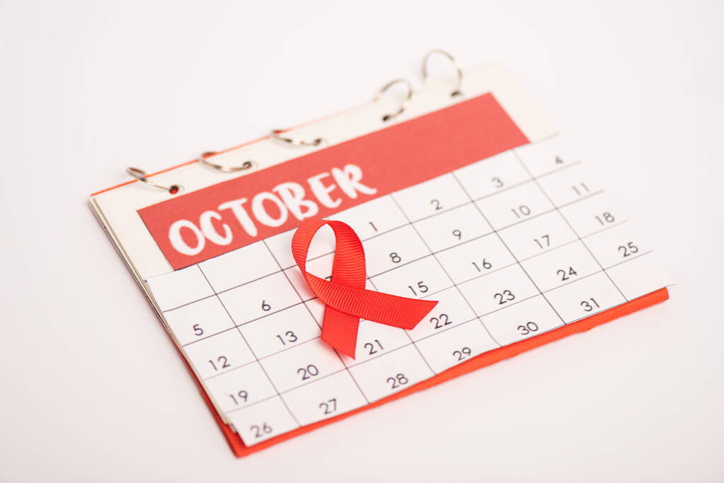 Selektywne skupienie czerwonej wstążki świadomości AIDS na kalendarzu października izolowane na białym - Zdjęcie, obraz
