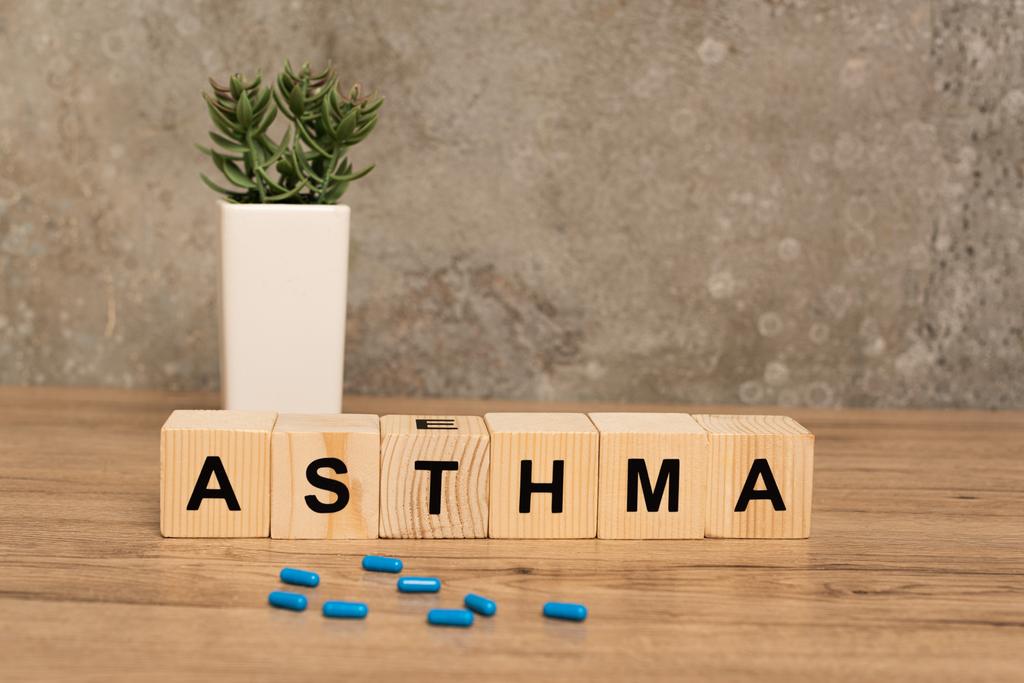 Вибірковий фокус таблеток і дерев'яних кубиків з астмою, що розкладається біля рослини на дерев'яному столі на сірому фоні
 - Фото, зображення