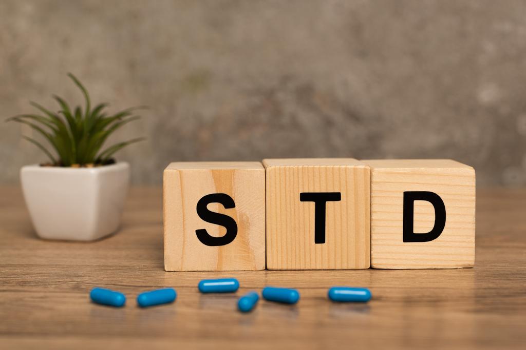 Selective focus of blocks with std letters, pills and plant on wooden table on grey background - Photo, Image
