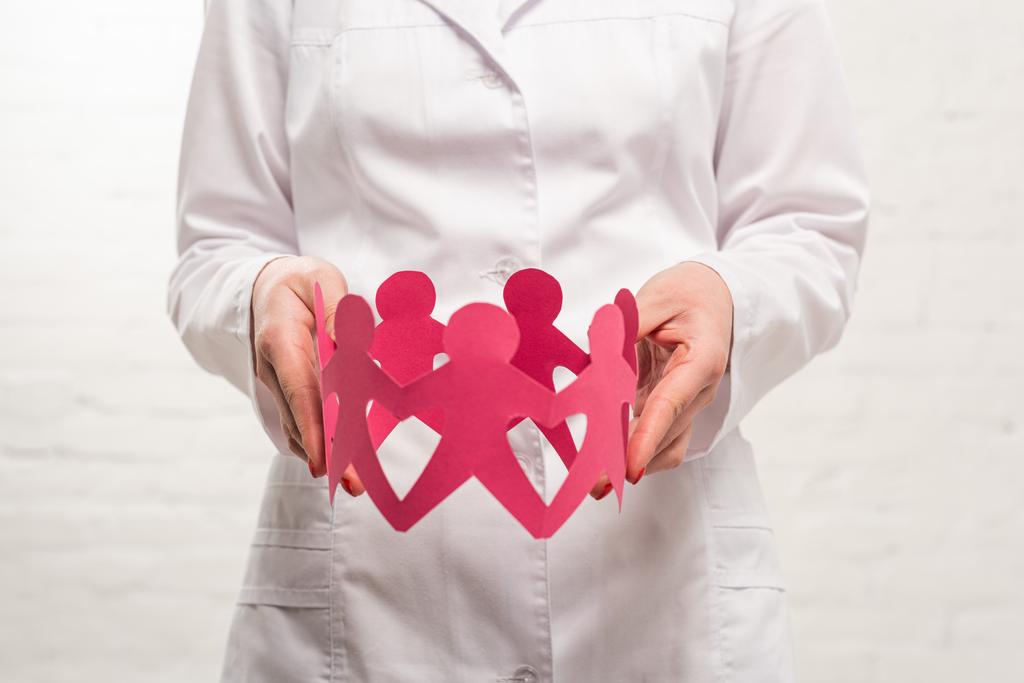 Cropped view of doctor holding paper figures of people on white background - Photo, Image