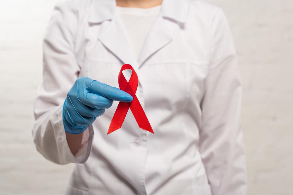 Vista recortada del médico en guante de látex con cinta roja de sida conciencia sobre fondo blanco
 - Foto, imagen