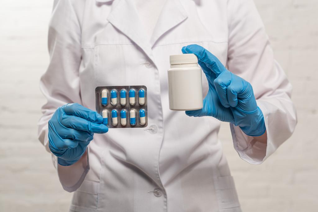 Vista cortada de médico segurando frasco e blister com pílulas em fundo branco
 - Foto, Imagem