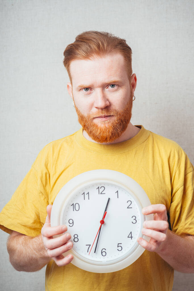 sur un fond gris homme avec une barbe en chemise jaune tenant une horloge et effrayé
 - Photo, image