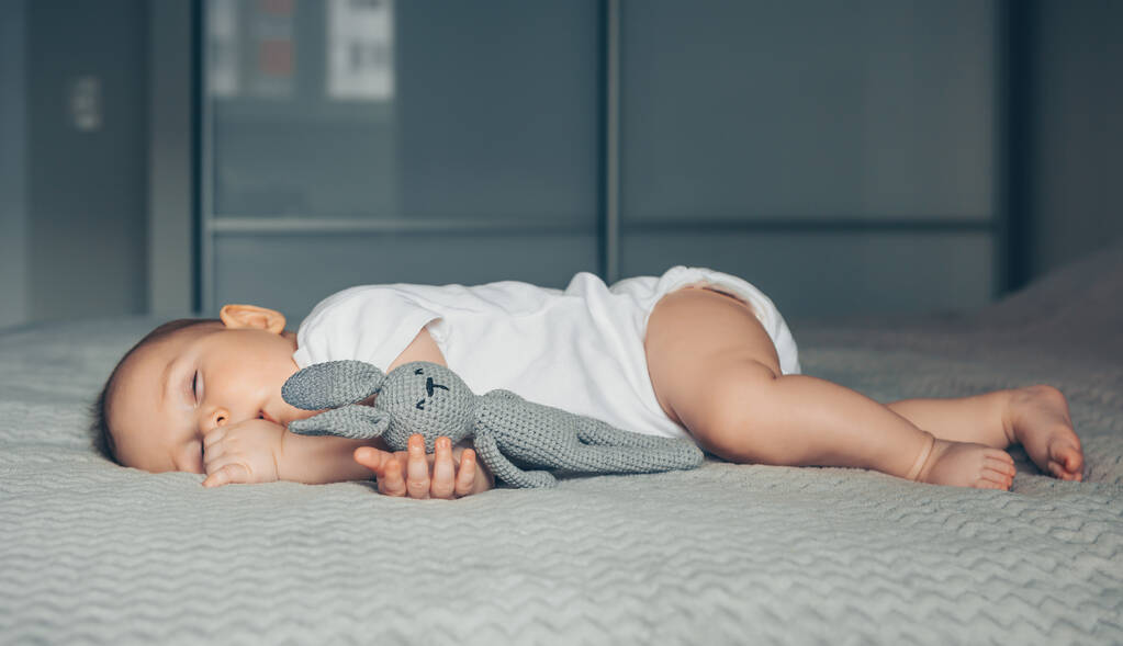 Édes újszülött alszik egy szürke játék nyúl az ágyon - Fotó, kép