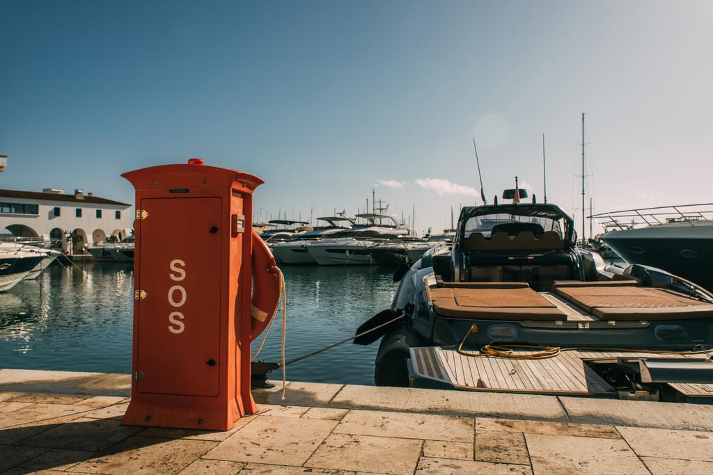 cabine vermelha com sos lettering perto de iates no mar Mediterrâneo
 - Foto, Imagem