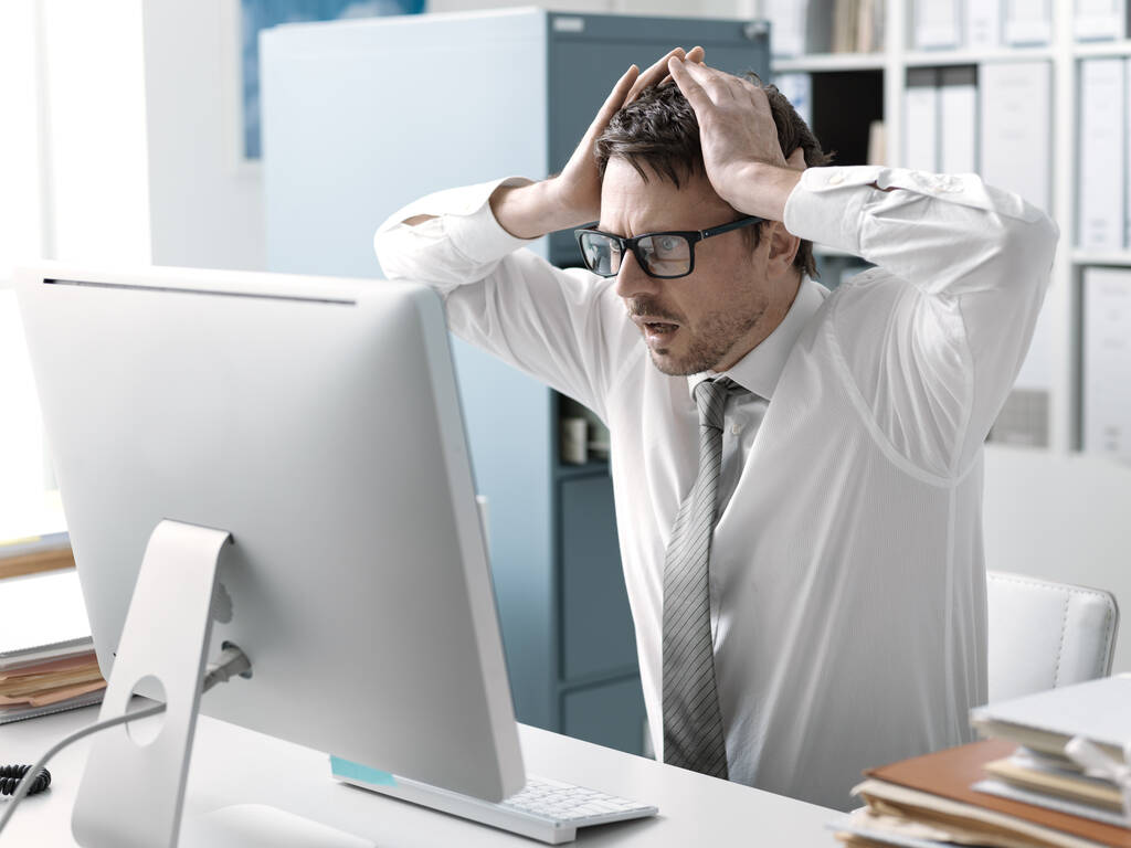 Панікуючий бізнесмен з головою в руках у своєму офісі, він отримує шокуючі погані новини на своєму комп'ютері
 - Фото, зображення