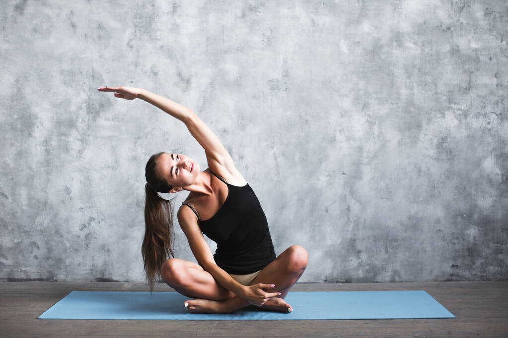 Joven mujer morena haciendo ejercicio sobre una colchoneta de fitness fotografiada al estirar el brazo
 - Foto, Imagen