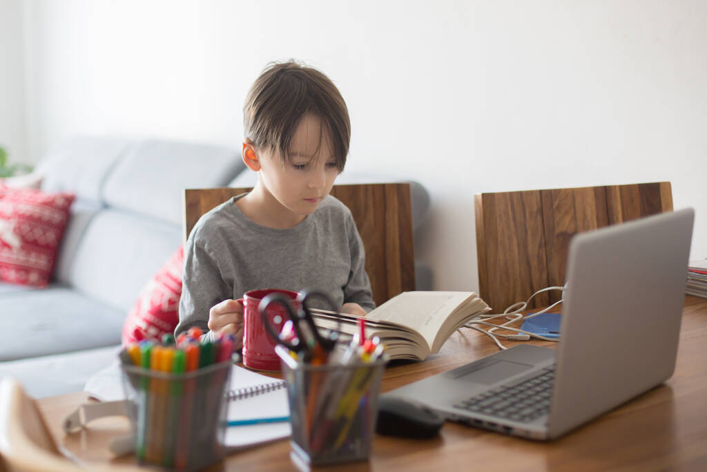 Bambino della scuola, seduto al tavolo con il computer portatile, scrivere compiti scolastici mentre la scuola a casa, mentre la scuola chiusa a causa di Coronavirus - Foto, immagini