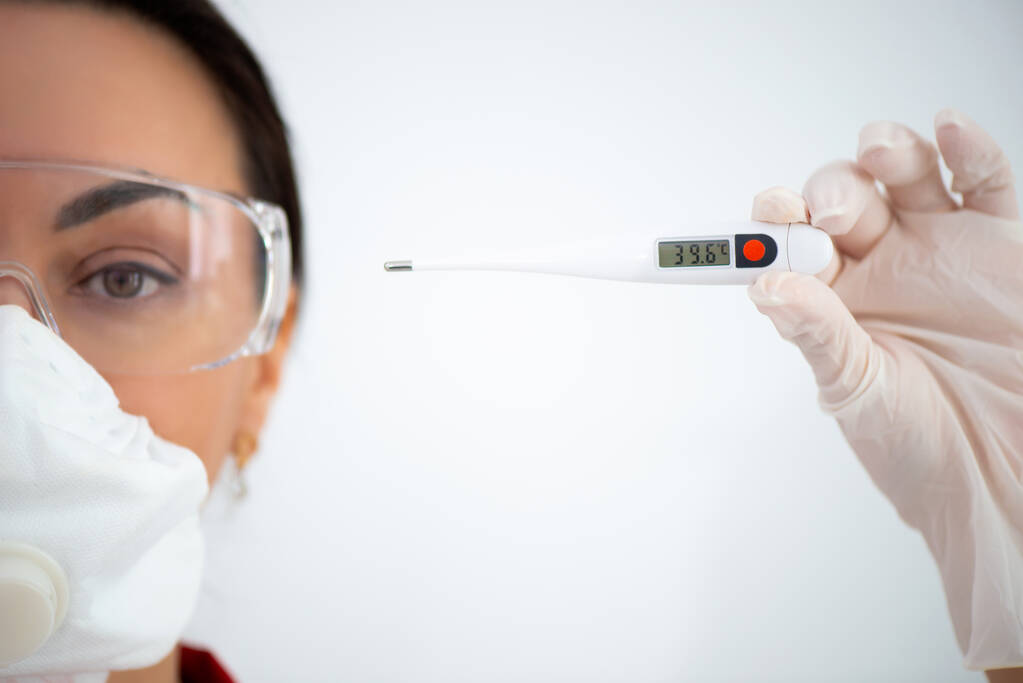 Лікар у окулярах і хірургічній масці тримає електронний термометр для вимірювання температури. Ознаки грипу COVID 19 Коронавірус. - Фото, зображення