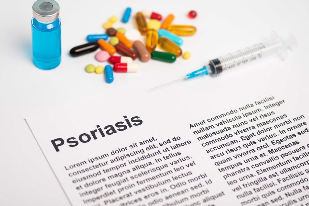 Papier avec lettrage psoriasis près du pot, de la seringue et des pilules sur fond blanc - Photo, image