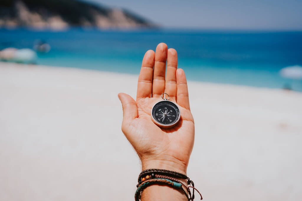 Розтягнута рука долоні з чорним металевим компасом проти літнього пляжу і блакитного моря. Дотримуйтесь свого шляху, мети, концепції бажань. Точка зору pov
 - Фото, зображення