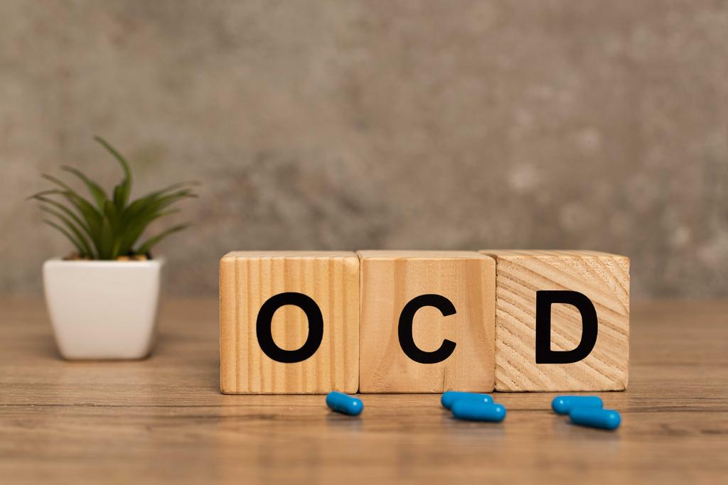 Focus selettivo di lettere ocd su cubi vicino pillole e pianta su superficie di legno su sfondo grigio
 - Foto, immagini
