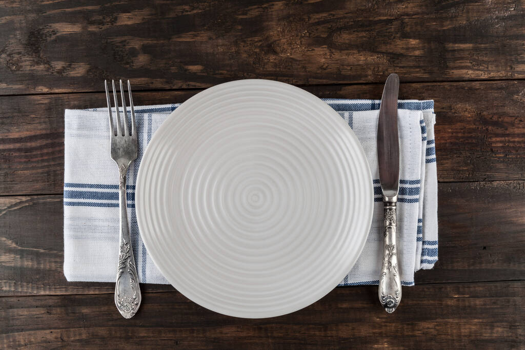 Tischdecke mit weißem Teller, Vintage Messer und Gabel, Geschirrtuch auf Holztisch. Draufsicht mit Kopierraum. - Foto, Bild