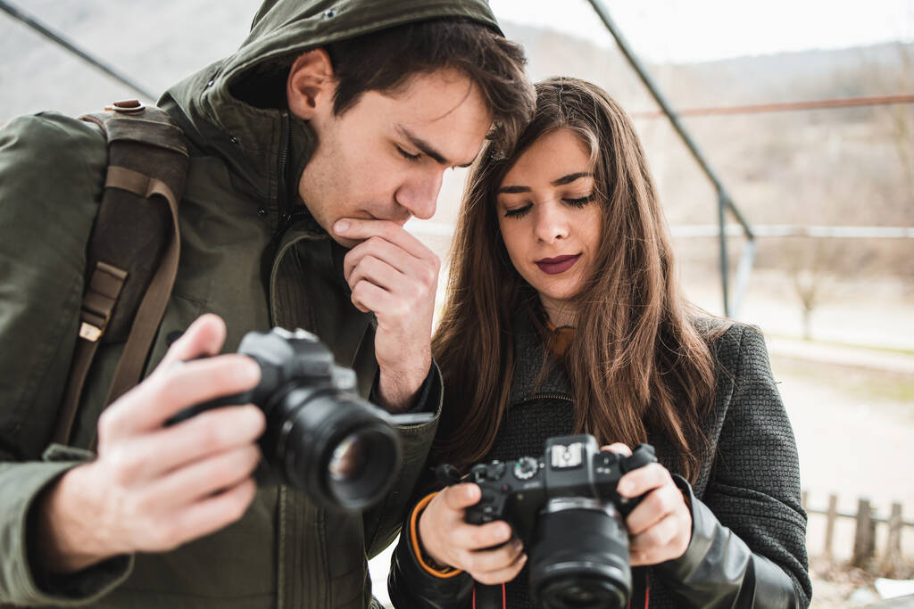 Kameraları olan güzel, genç bir çift fotoğrafçı. Kız arkadaşı erkek arkadaşına fotoğraflarını gösteriyor. - Fotoğraf, Görsel