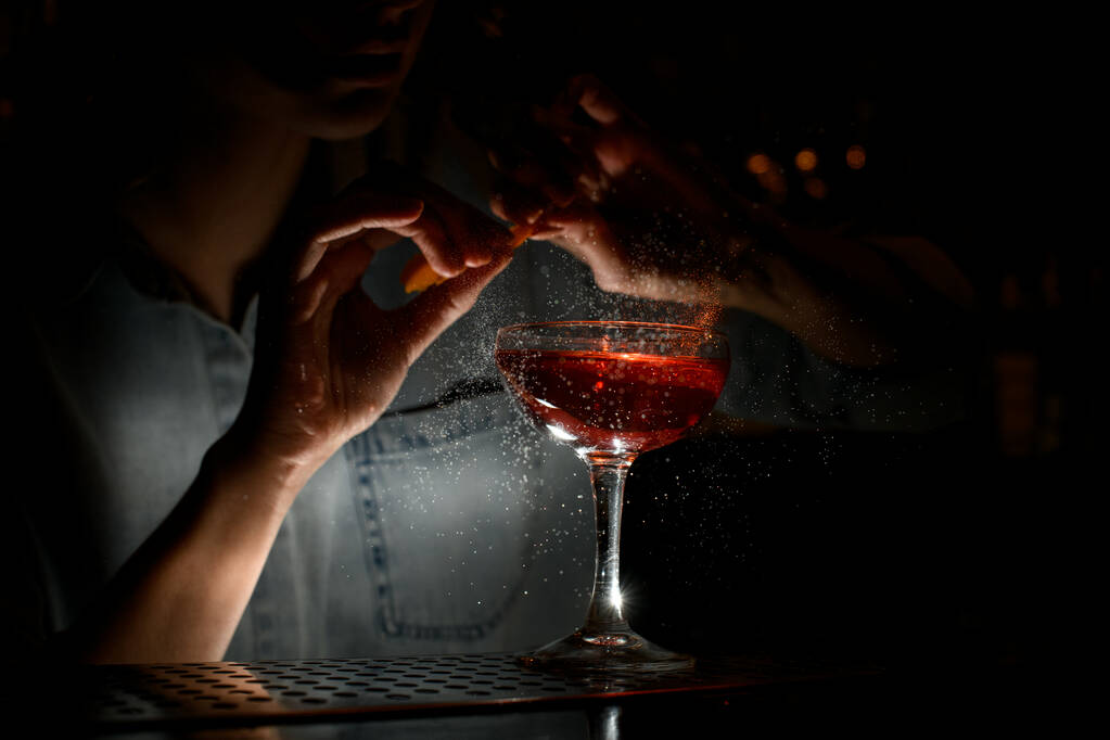 Barfrau streut an Bar vorsichtig Zitrussaft auf Weinglas mit Cocktail - Foto, Bild