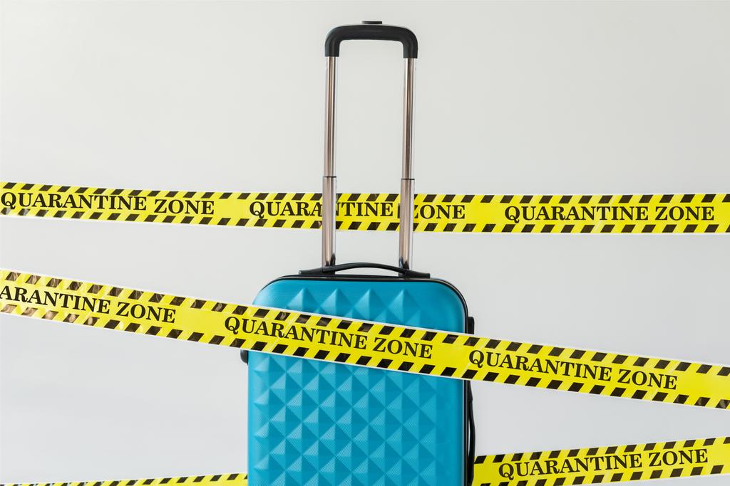 μπλε βαλίτσα σε κίτρινη και μαύρη ταινία ασφαλείας προειδοποίησης κινδύνου με απεικόνιση ζώνης καραντίνας που απομονώνεται σε λευκό, έννοια coronavirus - Φωτογραφία, εικόνα
