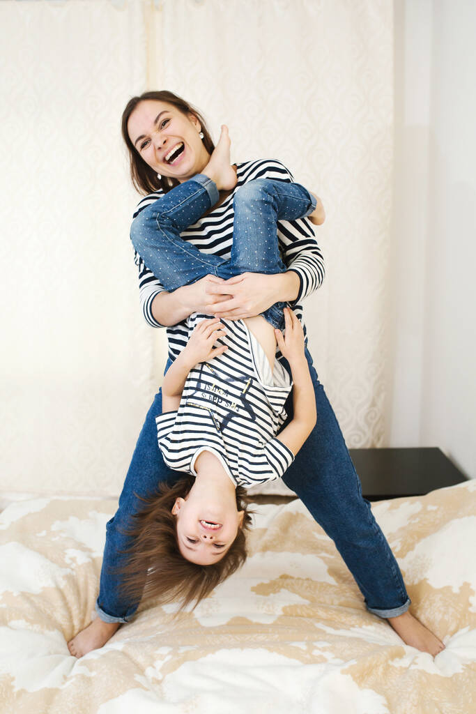 Fiatal boldog anya szórakozás vele aranyos kis baba tartja őt fejjel lefelé, játék és nevetés, aktív játékok otthon, teljes test - Fotó, kép