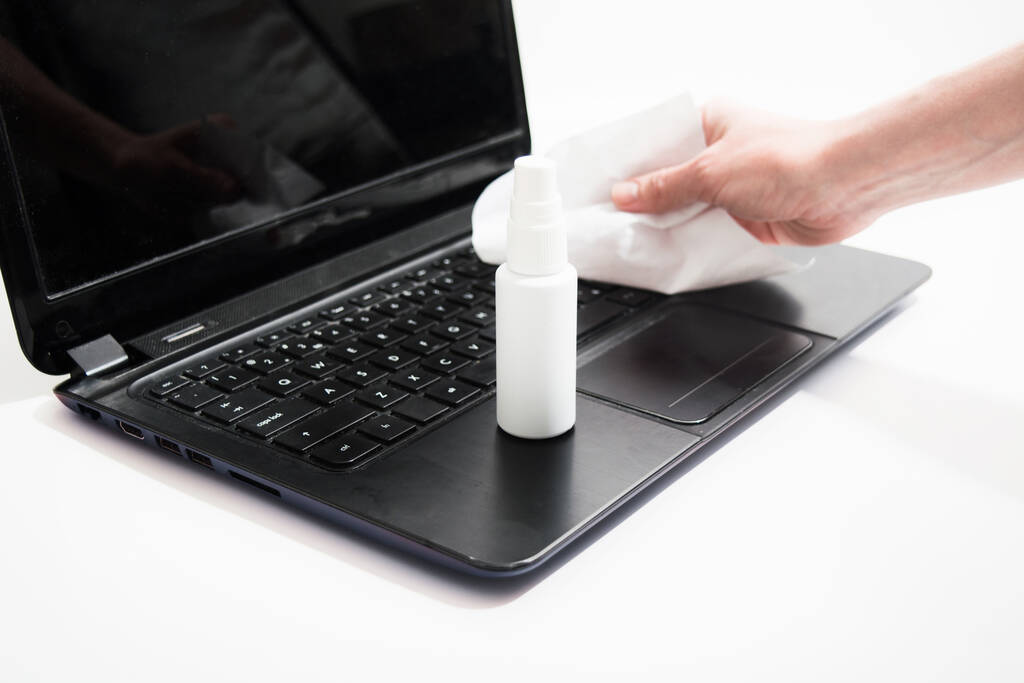 Woman hand wipe laptop with liquid for cleaning and prevention of virus on white background. Selective focus on bottle with sanitizer - Photo, Image