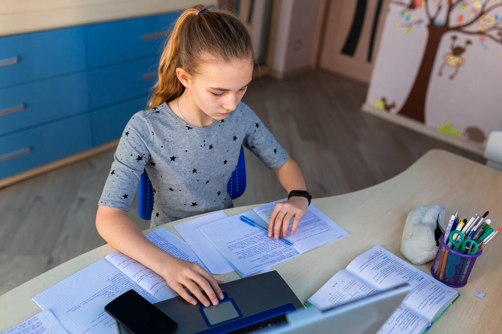 Beautiful young school girl working at home in her room with a laptop and class notes studying in a virtual class. Distance education and learning, e-learning, online learning concept during quarantine - Photo, Image