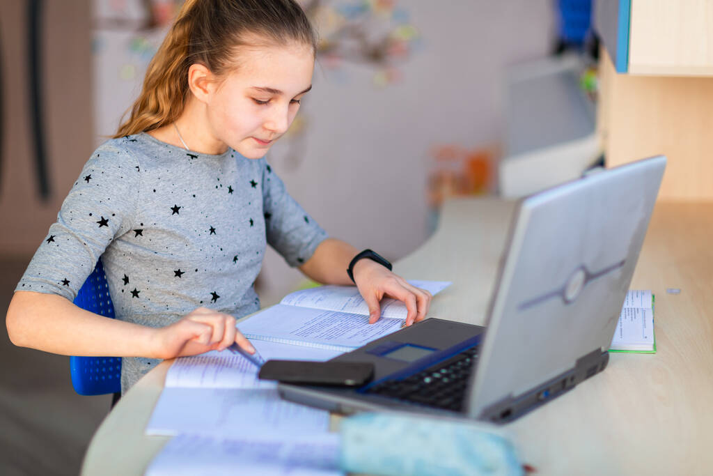 Piękna młoda uczennica pracująca w domu z laptopem i notatkami klasowymi studiująca w klasie wirtualnej. Kształcenie i uczenie się na odległość, e-learning, koncepcja uczenia się przez Internet podczas kwarantanny - Zdjęcie, obraz