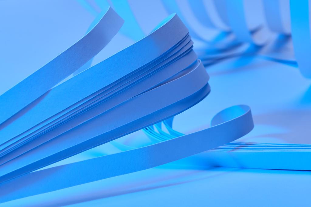 Neon mavi arkaplan üzerindeki kavisli kağıt şeritlerinin görünümünü kapat - Fotoğraf, Görsel