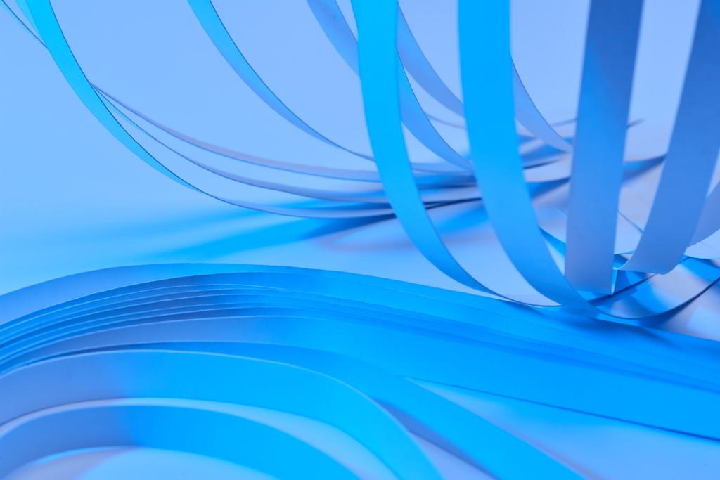 κοντινή προβολή καμπυλωτών λωρίδων χαρτιού σε μπλε φόντο νέον - Φωτογραφία, εικόνα