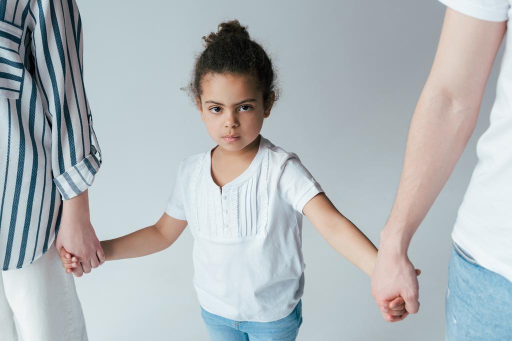 adoptowane afrykańskie amerykańskie dziecko trzymające się za ręce z rozwiedzionymi rodzicami odizolowanymi na szaro   - Zdjęcie, obraz