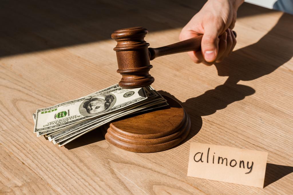 vista recortada del juez sosteniendo martillo cerca de billetes de dólar y papel con letras de pensión alimenticia en el escritorio
 - Foto, imagen