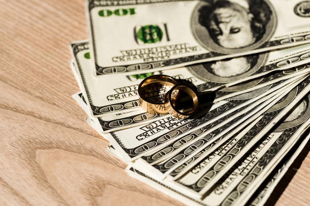τραπεζογραμμάτια δολαρίων κοντά σε χρυσά δαχτυλίδια εμπλοκής σε ξύλινη επιφάνεια  - Φωτογραφία, εικόνα