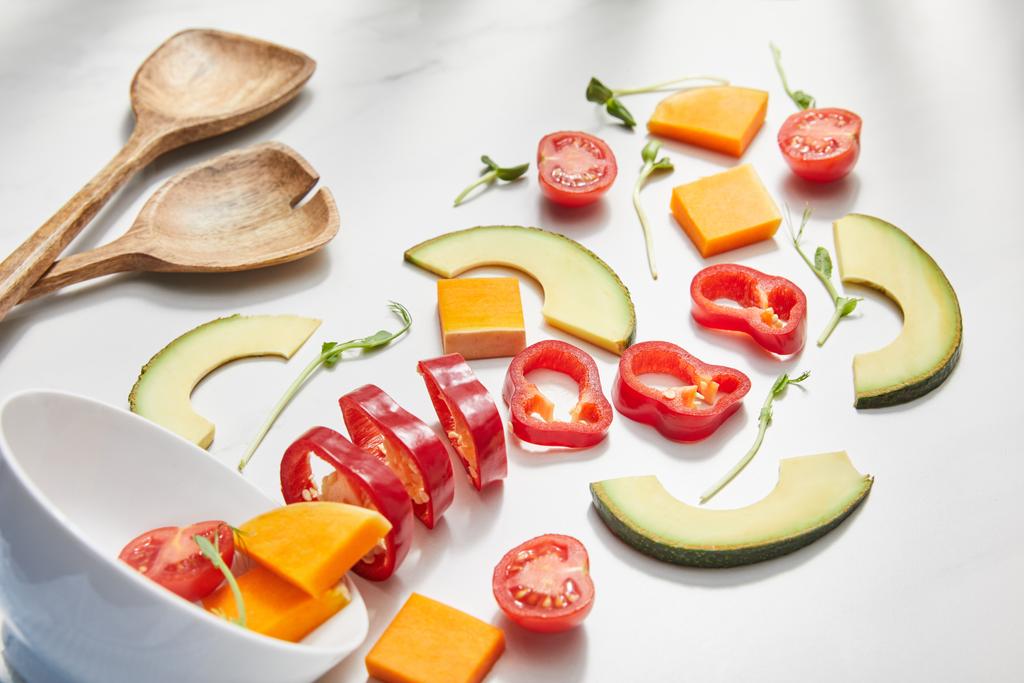 Vista di angolo alto di boccia con microverdi, verdure di taglio e fette di avocado vicino a spatole su bianco
  - Foto, immagini