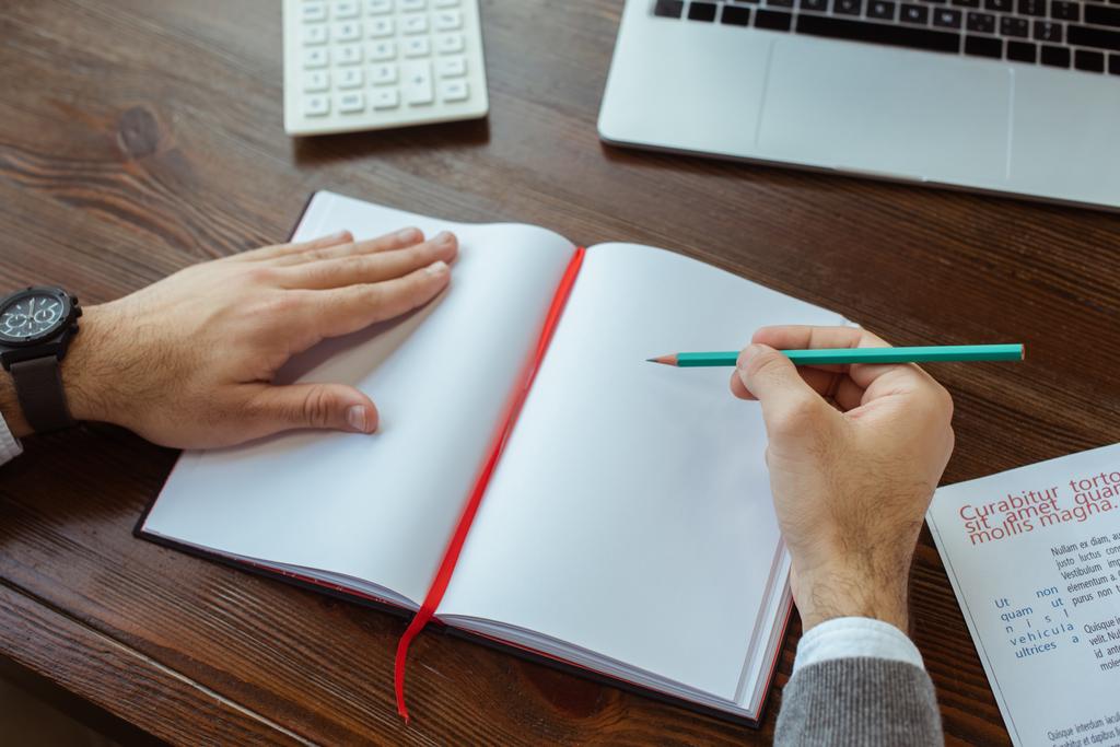 Částečný pohled na podnikatele psaní v notebooku u notebooku a kalkulačky u stolu v kanceláři - Fotografie, Obrázek