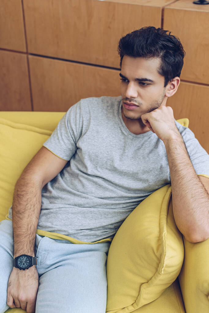 Задумчивый мужчина на желтом диване в гостиной
 - Фото, изображение