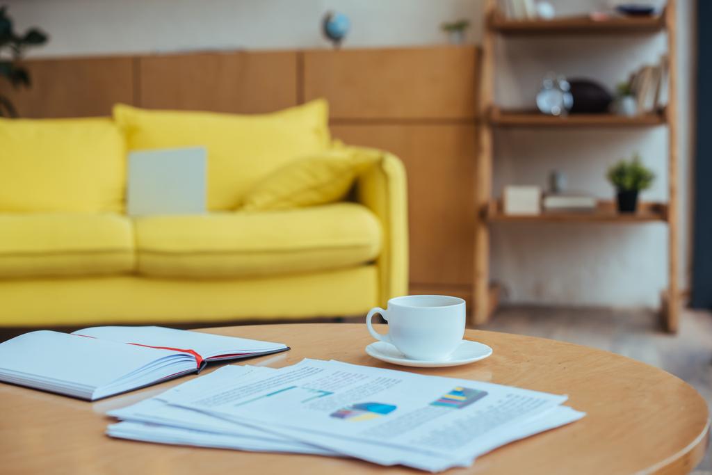 Stolik kawowy z papierami, filiżanka kawy i notatnik w salonie - Zdjęcie, obraz