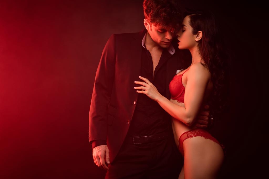 beautiful passionate couple hugging on black with red light - Photo, Image