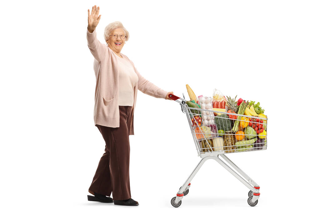 Eine ältere Frau mit einem Einkaufswagen winkt isoliert auf weißem Hintergrund in voller Länge in die Kamera - Foto, Bild