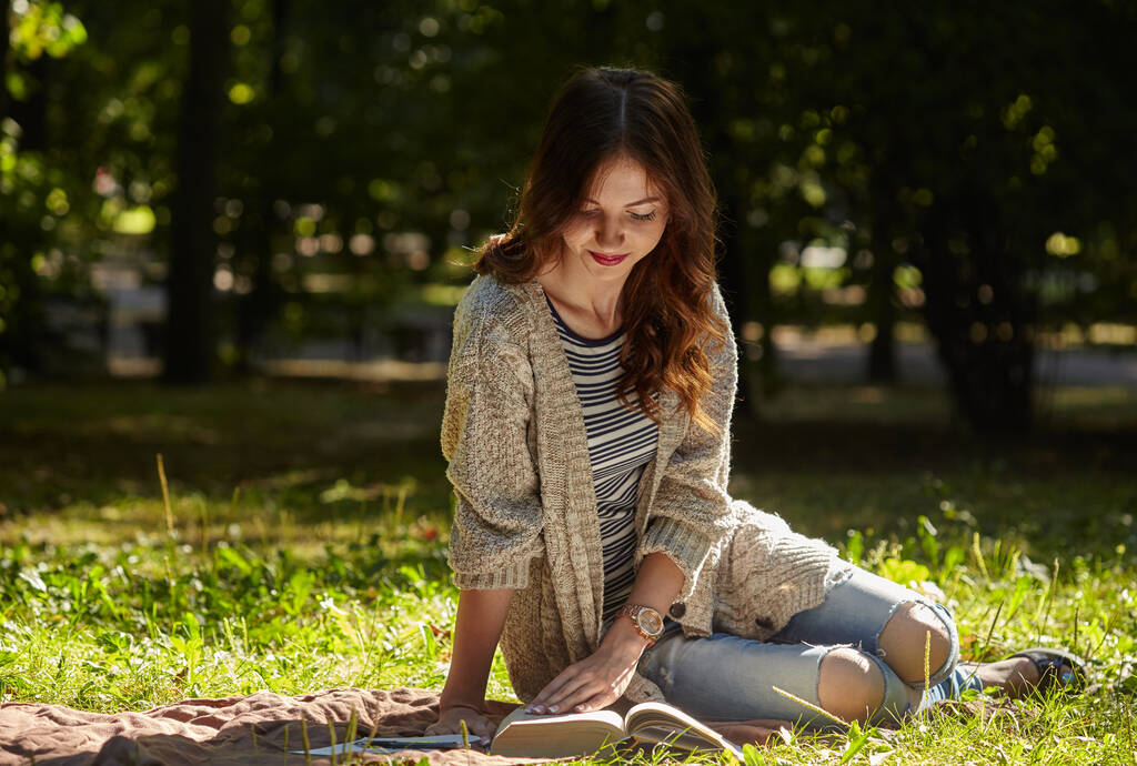 Genç bir kadın sessiz yeşil çimenlerde oturuyor ve kitap okuyor. - Fotoğraf, Görsel