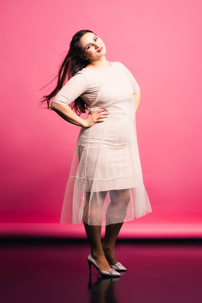 Modelo de talla grande con cabello largo soplando en el viento, mujer gorda sobre fondo rosa, concepto positivo para el cuerpo
 - Foto, imagen