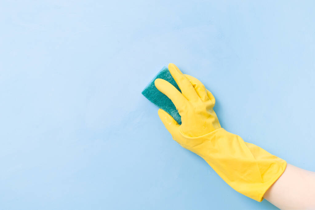 uma mão em uma luva de borracha amarela segura uma esponja amarela com um lado áspero verde para limpar sujeira complexa, espaço de cópia de fundo azul, conceito de limpeza, cuidados domésticos, limpeza de primavera
 - Foto, Imagem